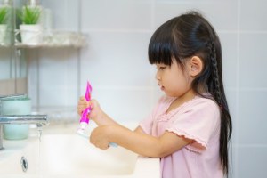 A little girl putting toothpaste on her toothbrush. 