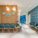 Waiting area with rows of teal chairs, wood-paneled walls, hanging cloud lights, and colorful underwater-themed hallway in background.
