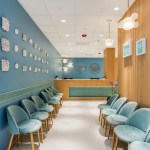 Symmetrical view of waiting room with teal chairs lined along both sides, leading to reception desk under soft pendant lighting.