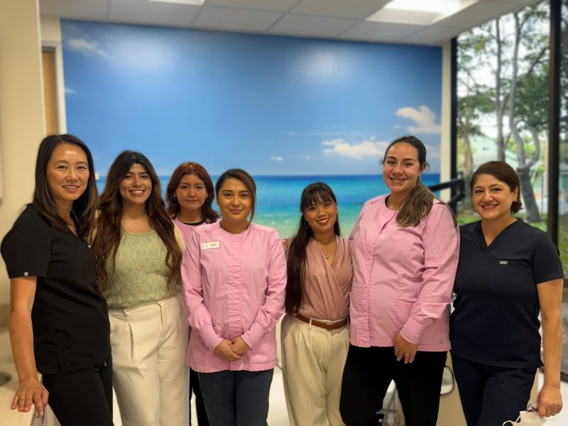 Group of seven dental team members posing together in front of a calming ocean mural inside the clinic.